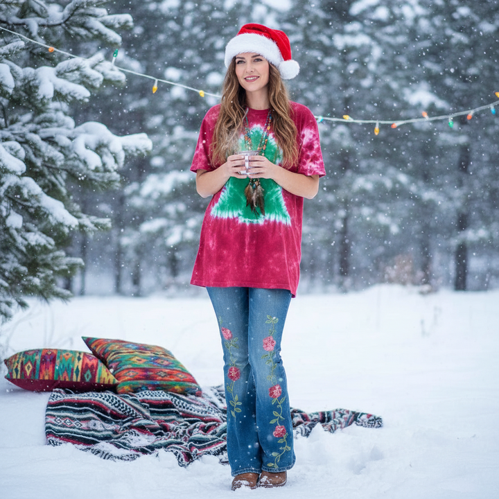 Woman in a tie-dye shirt and Santa hat standing in a snowy forest with colorful pillows and blankets.